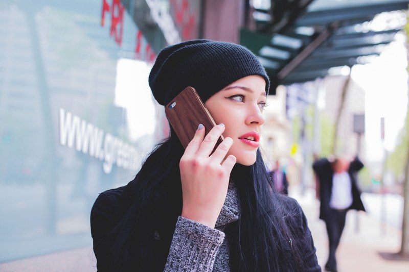 a young woman in a beanie talking on a phone while standing on a sidewalk, on a phone on a sidewalk 4k