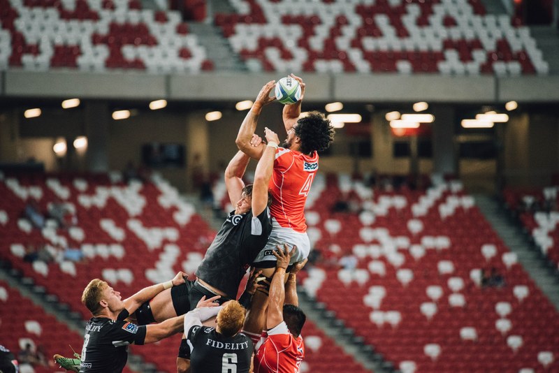 a shot of two rugby players jumping high for a ball as other players make a rush, catching the ball 4k