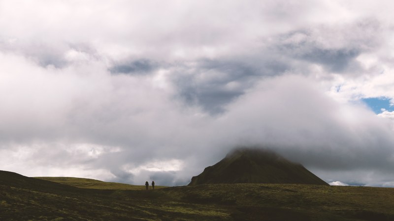 two people hiking across grassy plain underneath cloudy sky, a journey from another world 4k
