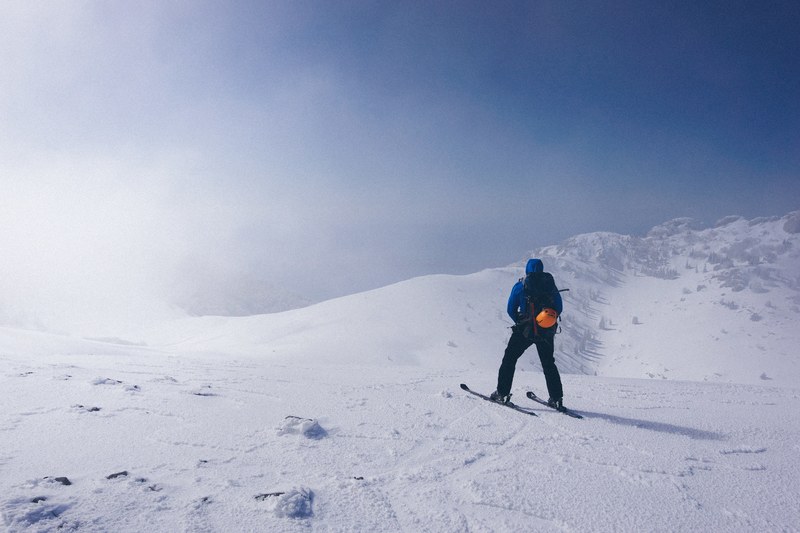 a man walking in skis on a slight slope near medium sized mountains, blown 4k