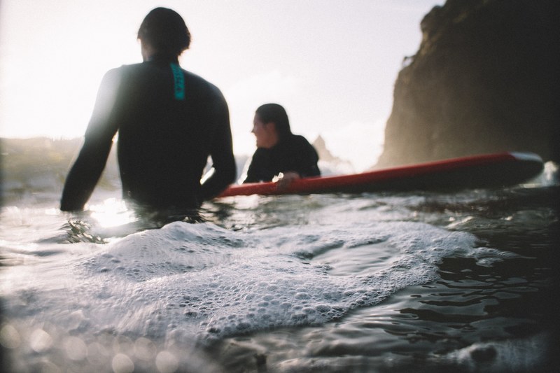 two surfers in wetsuits with a surfboard in the foamy ocean at piha beach, relaxing surfers at piha beach 4k