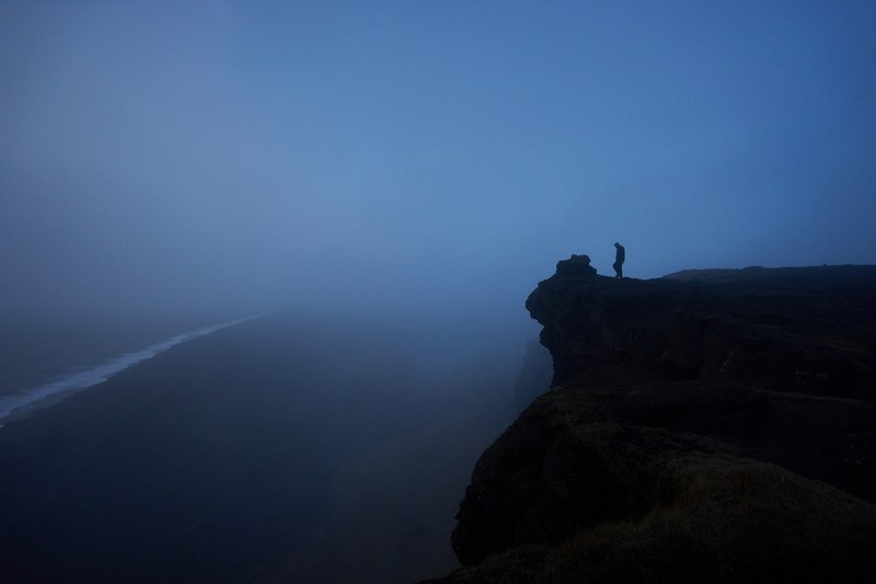 silhouette of person on a mountain ledge near a misty shore, safety third 4k