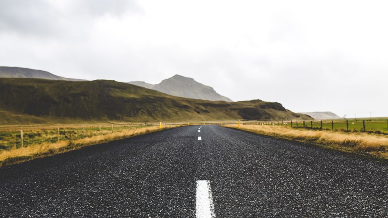 a low shot of an asphalt road running along flat hills in island, road through icelandic hills 4k