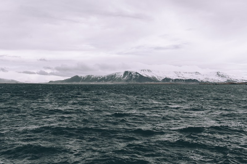 ocean around cloudy iceland with snow capped rocks and mountains at the horizon, rough waters in reykjavik 4k