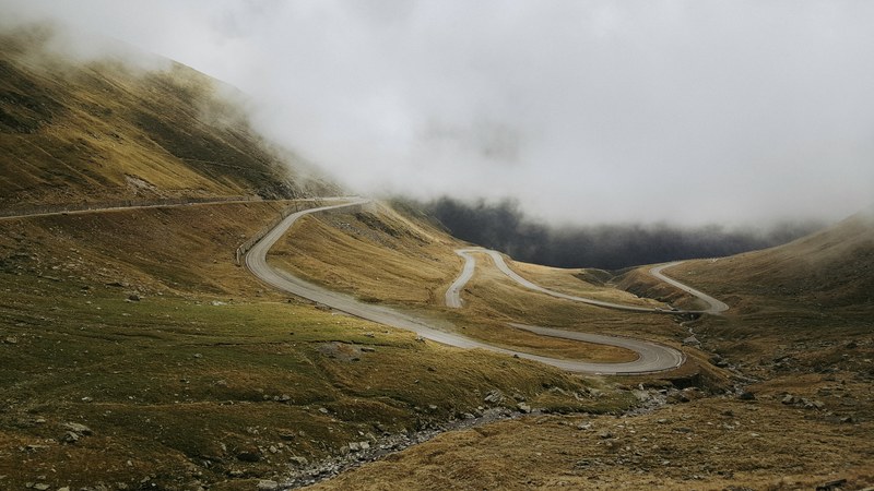 winding roads line the slopes of green foggy countrysides, transfagarasan 4k