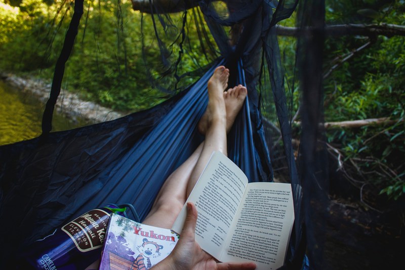 person relaxing in a hammock reading books and drinking water, hammock life 4k