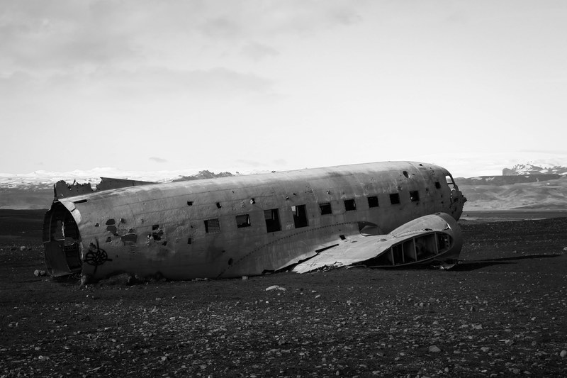 black and white picture of plane wreck on stony ground with mountains in background iceland, lift off 4k