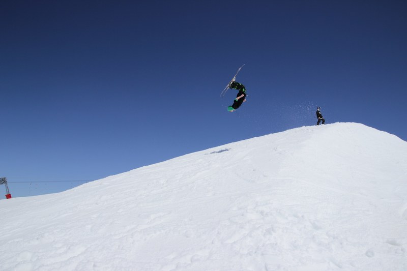 a skier upside down mid flip over a snowy hill against a clear blue sky, flipping skier 4k