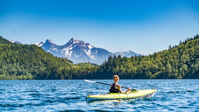 a woman in a kayak on a choppy lake with a view on tall snowy mountains, kayaking in the mountains 4k