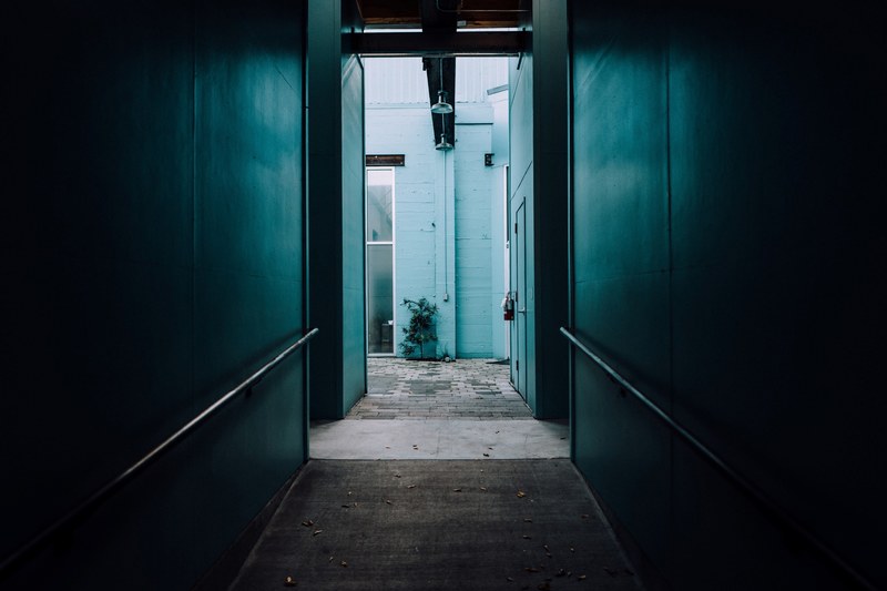 the corridor of a dark blue wall with hand railings on it in sonsie style, looking from dark to light 4k
