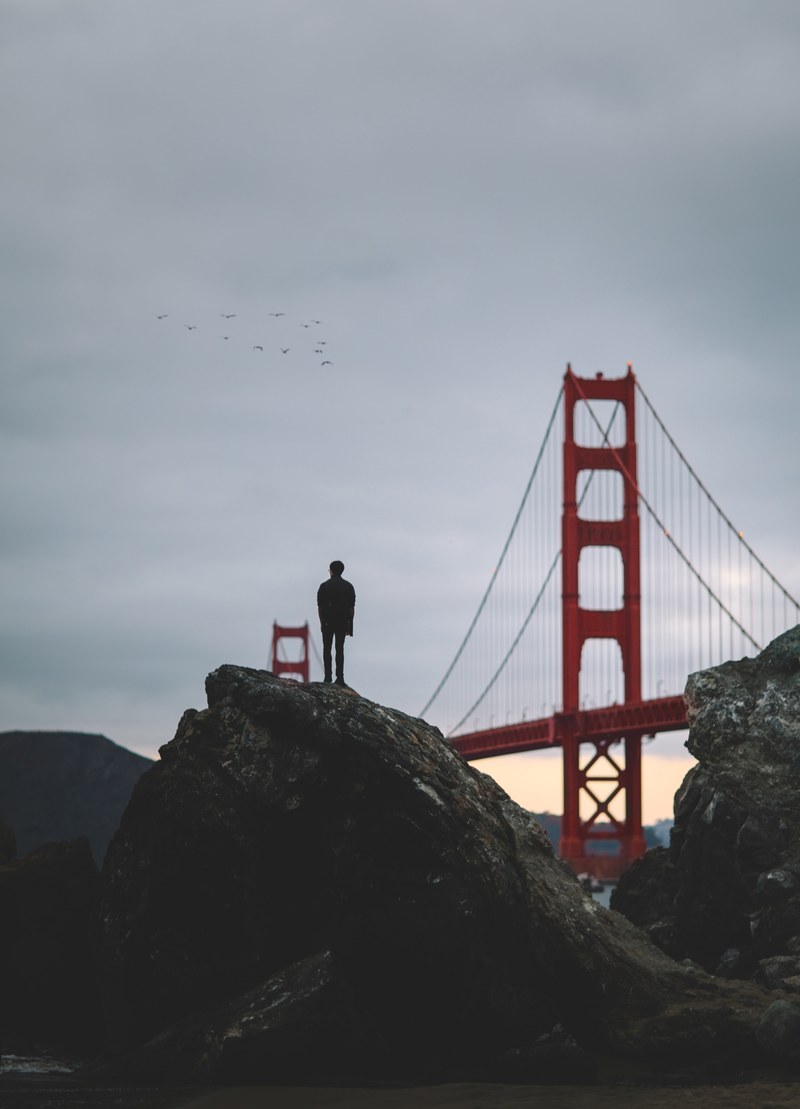 a lone person standing on a boulder looking towards the golden gate bridge, _marshalls beach 4k