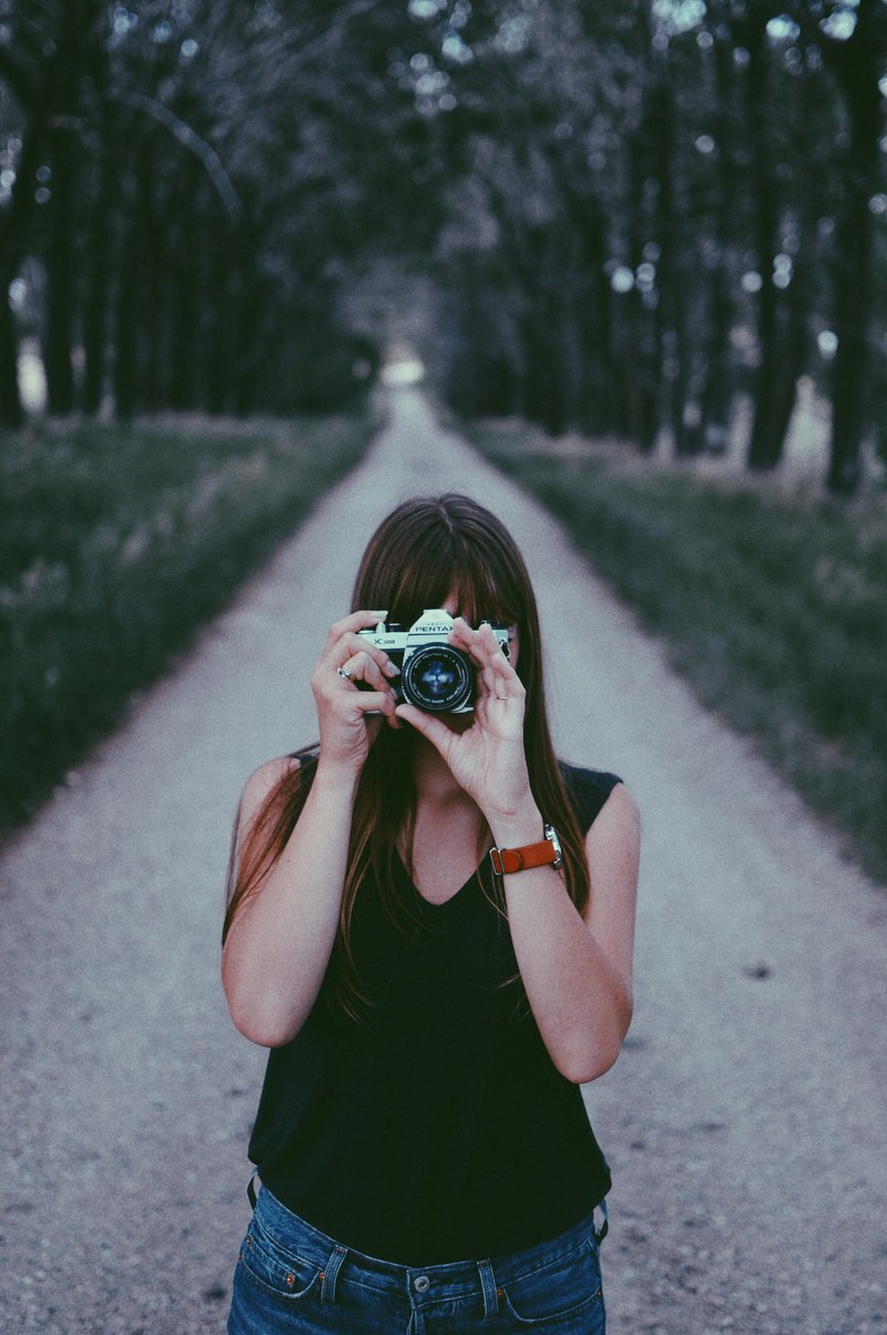 a woman standing in the middle of a dirt road and taking a photo with a camera, photographer on a dirt road 4k