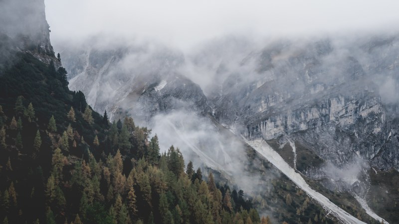 a fog descending from jagged mountain tops onto a forest in axamer lizum, mountain slopes under a mist 4k