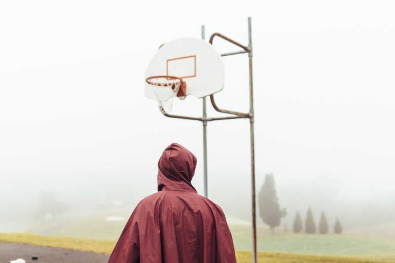 a man standing on an outdoor basketball court while wearing a jacket on a misty day in pembroke, basketball in the clouds 4k