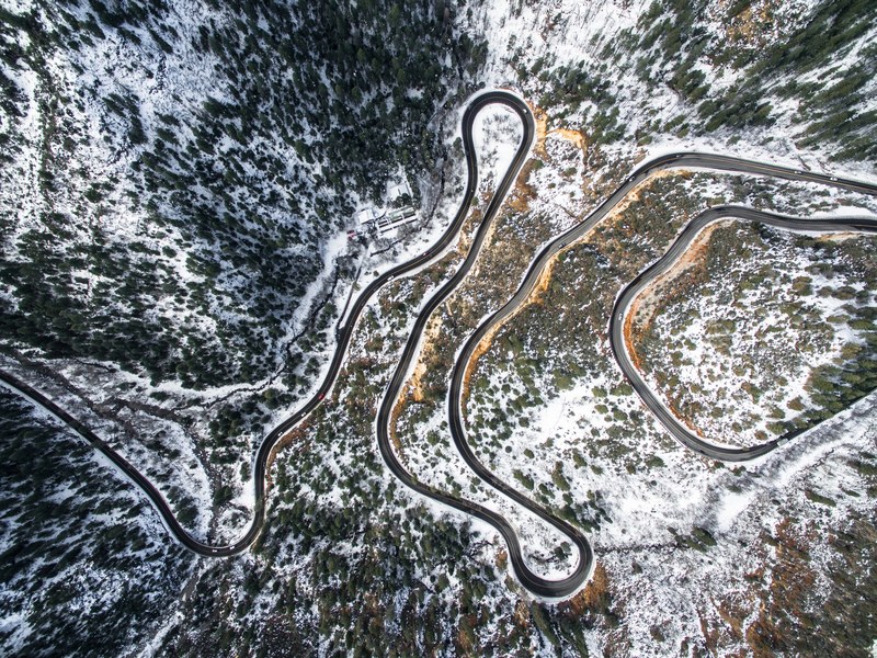 a drone shot of a winding asphalt road in a snowy forest, winding path 4k