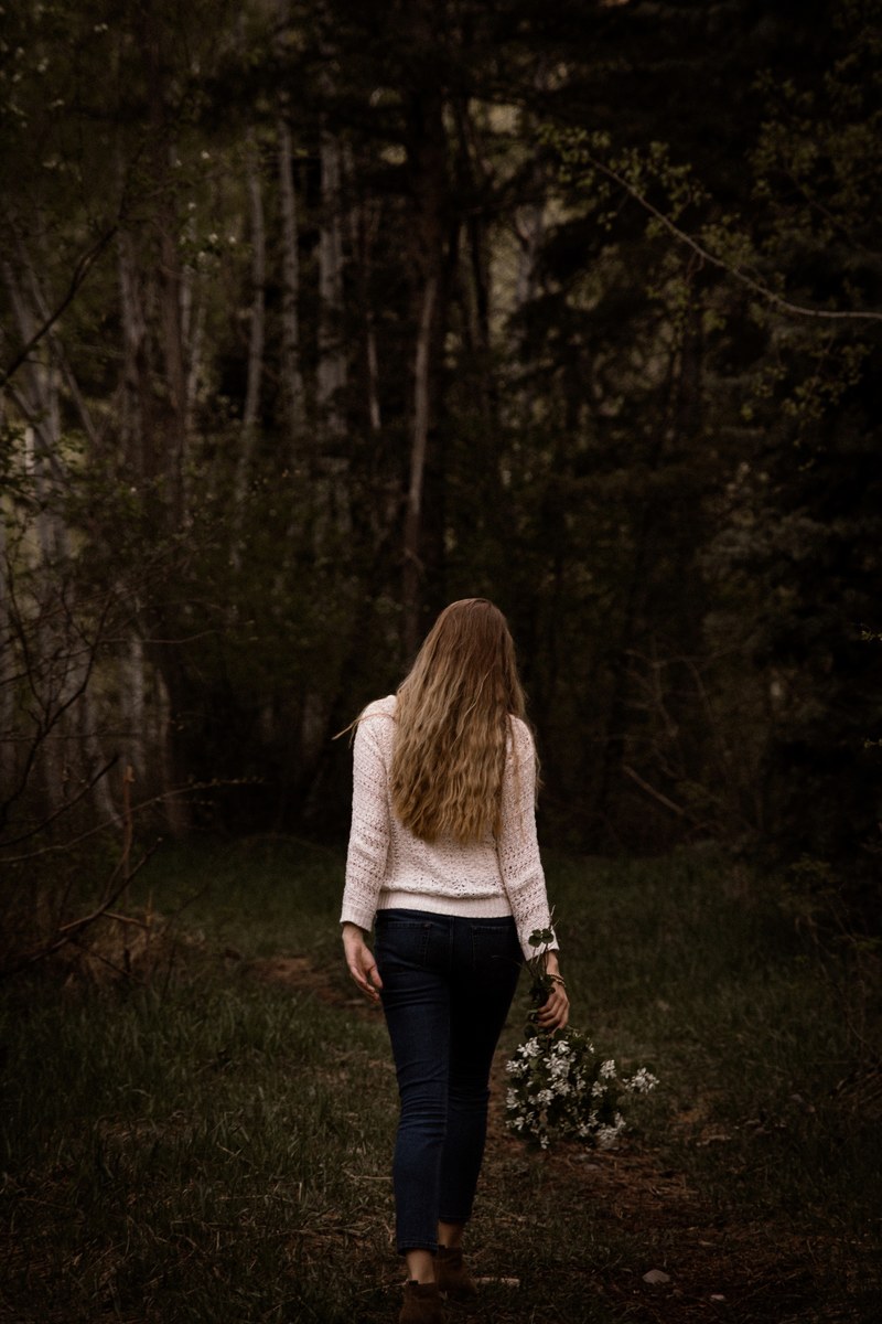 a lone woman with a bouquet of flowers in her hand walking on a forest trail, woman with flowers in the woods 4k
