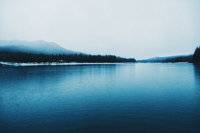 the surface of a lake in winter with a wooded hill on the foggy horizon, blue lake in the winter 4k
