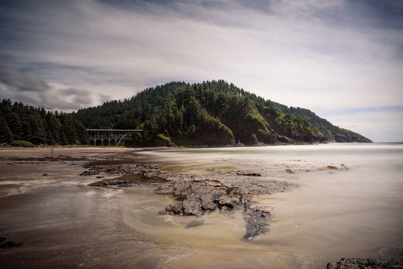 rocks and smooth sea water at the edge of a beach with an aqueduct in the background, aqueduct near a beach 4k