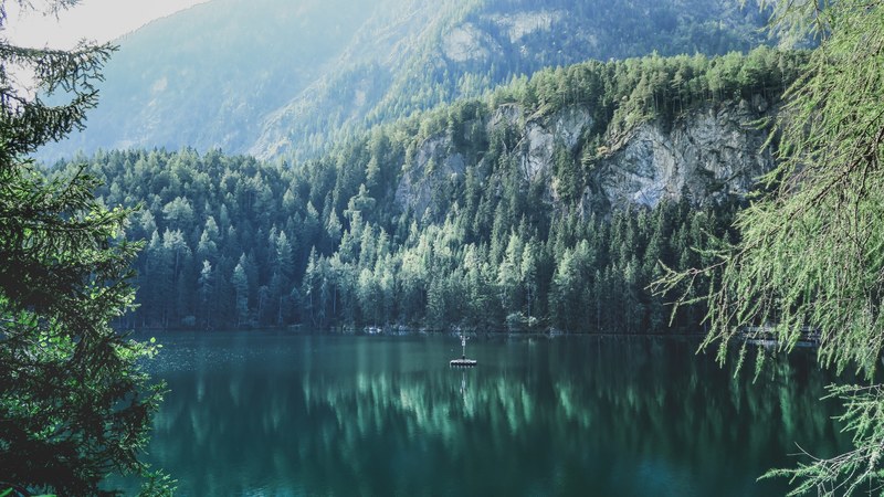 rocky slopes and woods overlooking the still surface of lake piburger see, green piburger see 4k