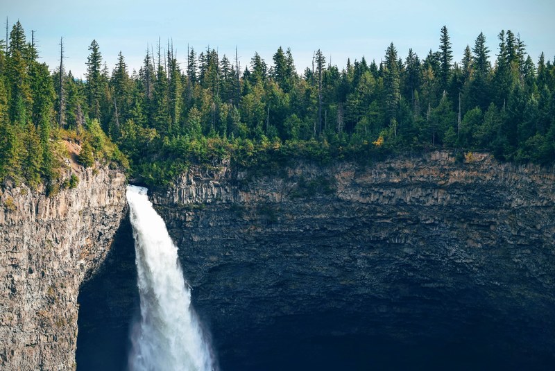 a tall waterfall tumbling down from a forested cliff, waterfall under a forest 4k