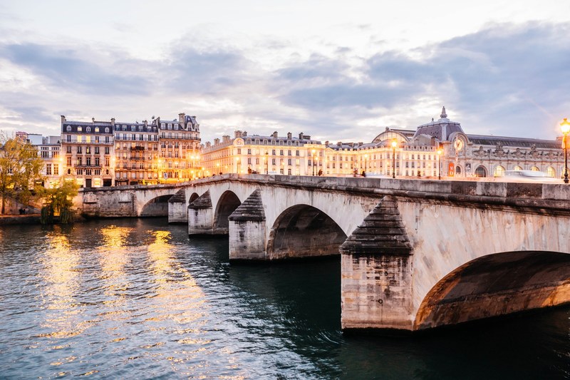 a bridge over the seine river with illuminated street lights and buildings behind, illuminated bridge on seine 4k