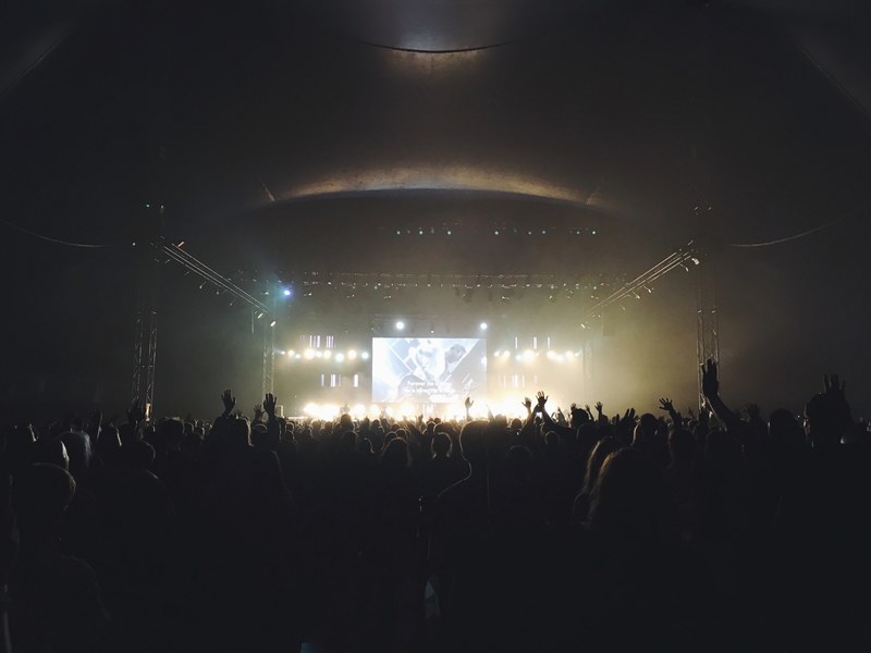 a shot from the back of a large concert audience with a large screen above the performing band, at the back of a concert venue 4k