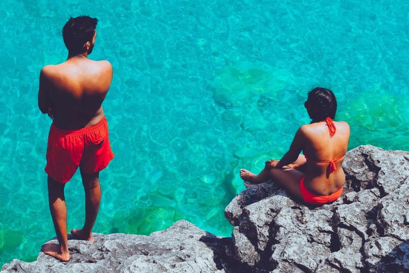 two people in swimsuits sit on a rock above blue water in the grotto, sitting above the grotto 4k