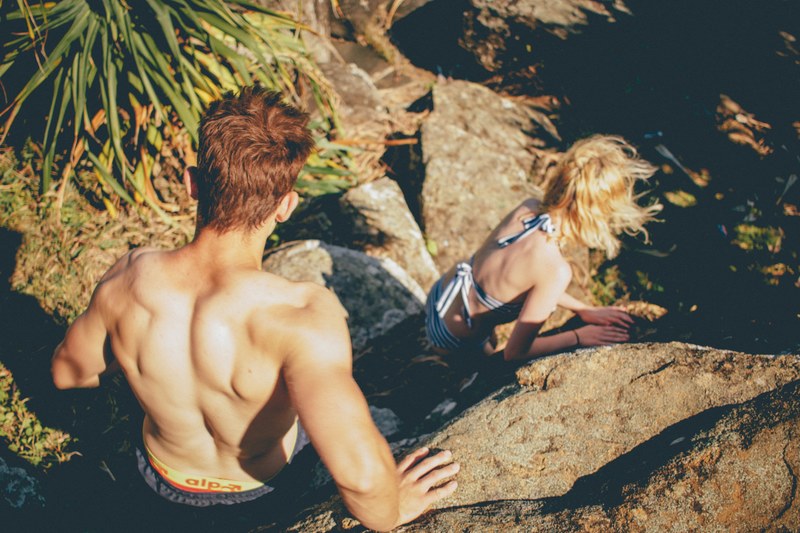 couple in swimwear climbing down the rocky cliff at kings beach, couple climbing down the cliff 4k
