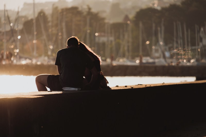 a couple sit on the harbour wall in quai gustave doret with boats in the background as the sun sets at dusk, _spring love 4k