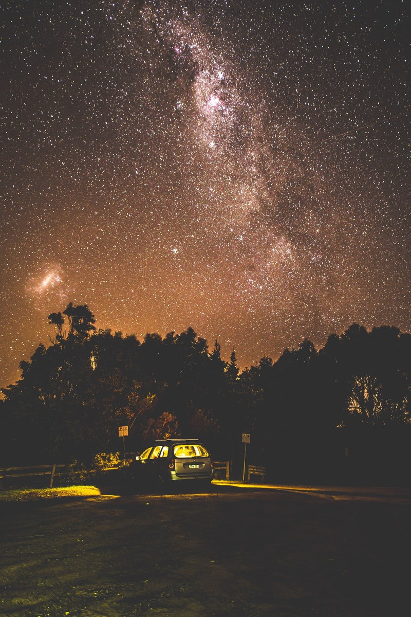 lights inside a car parked near a forest under a starry evening sky, the carpark 4k