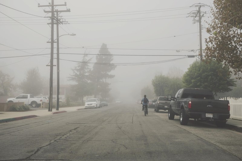 person bikes down a foggy suburban city street, biking on side streets 4k