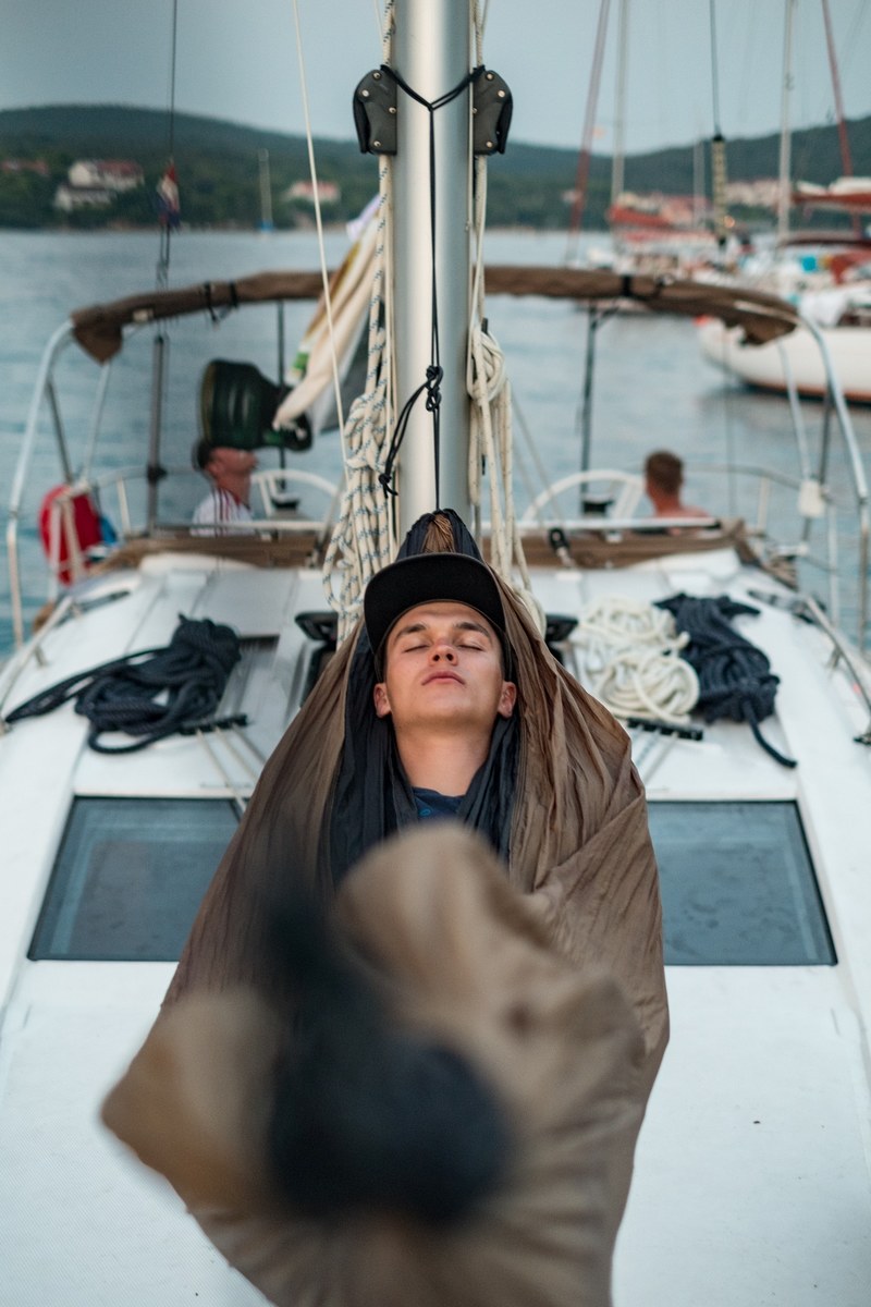 a man in a cap sleeps on a hammock rigged to the mast of a boat, sleepy skipper 4k