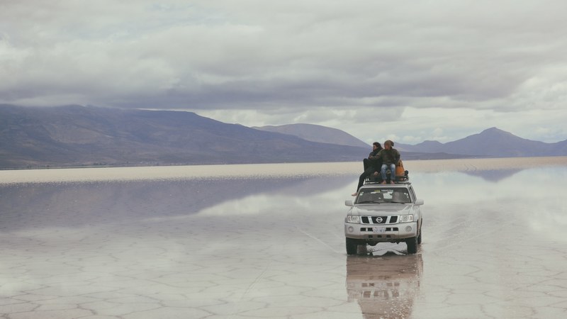two people sat on the roof of a silver nissan jeep on a salt flat uyuni, nissan jeep uyuni salt flat 4k