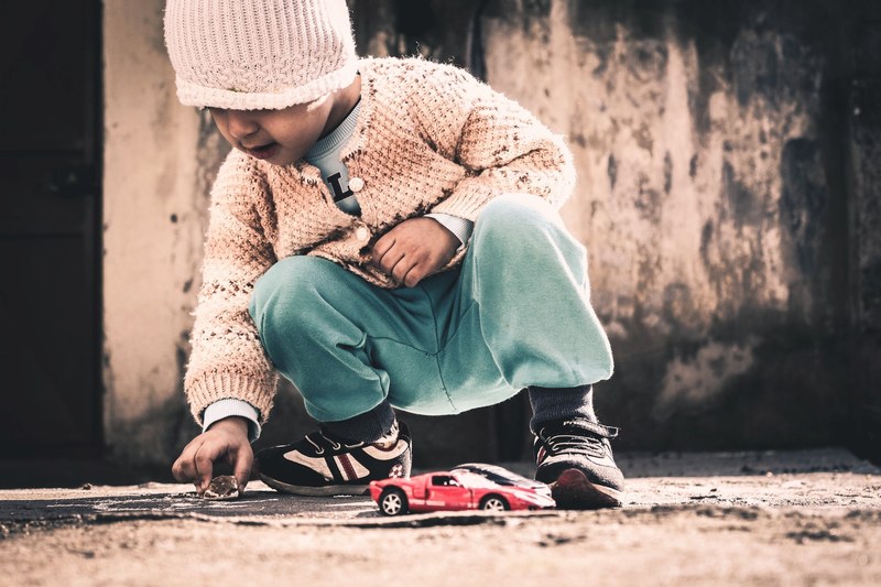 child in cardigan and hat playing outdoors with red toy car in onikiubat belediyesi, child outdoor face and playing 4k