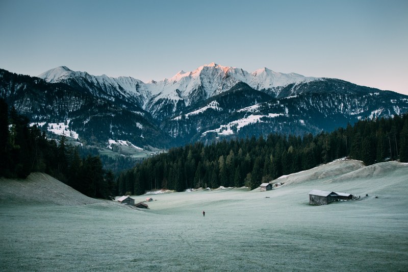 several wooden cabins on a slight slope with tall mountains on the horizon, cabins on a frozen slope 4k