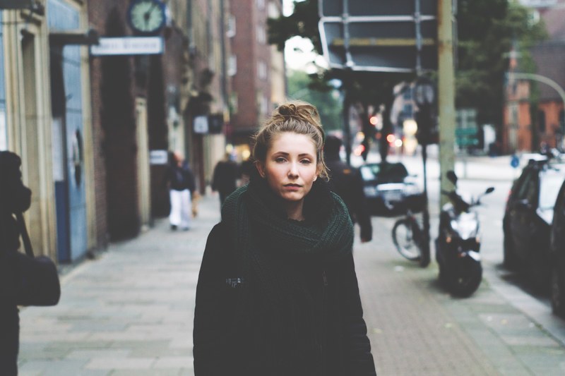 woman with a messy bun wearing a scarf and winter coat on a city street, lost in the city 4k