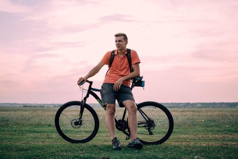 a man standing poised in a pink shirt in front of his bicycle in the country grass, man standing with bike 4k