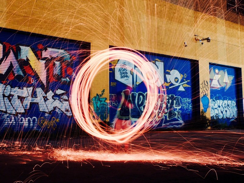 a firework light painting shot with wire wool taken in front of a building marked in graffiti, light painting circle in greenpoint 4k