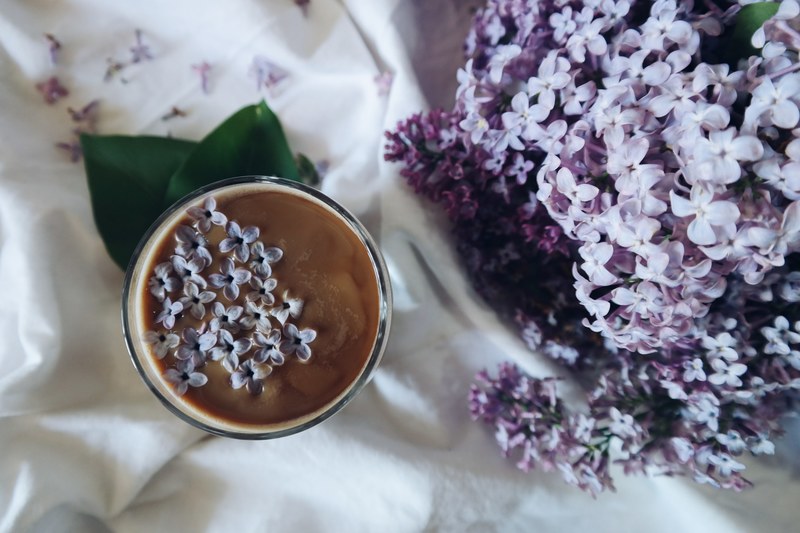 an overhead shot of a cup of coffee with small violet flowers on its surface, top view of floral coffee 4k