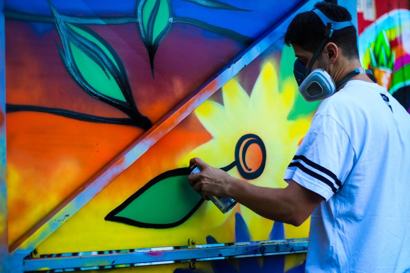 spray paint graffiti artist in t shirt with mask holding canister creating colorful wall mural, artist spray painting flowers 4k