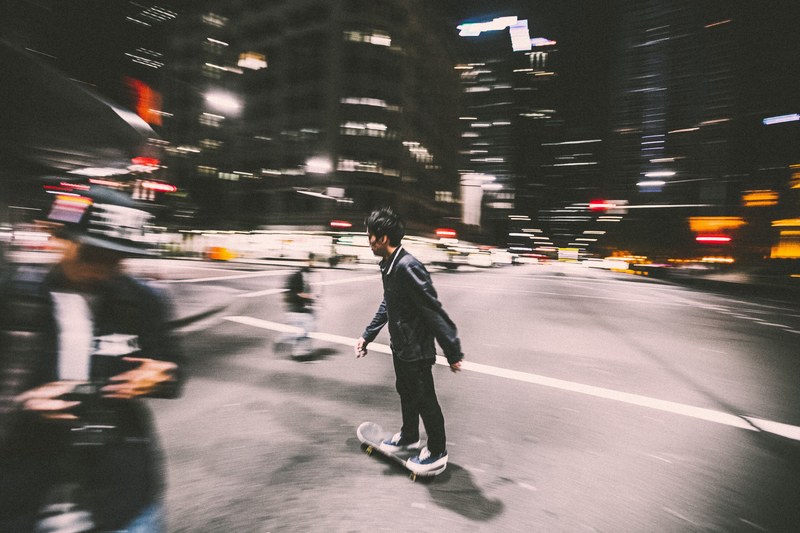 blurry photo of a man on skateboard in black jacket near an intersection in a city, skateboard intersection 4k