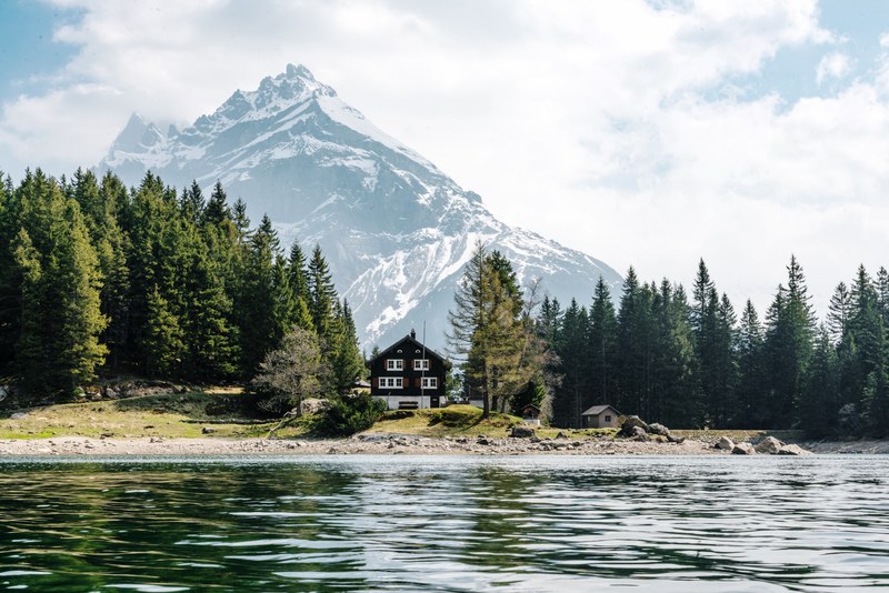 evergreens surround a cabin in arnisee switzerland while a snowy mountain top is in the distance, evergreen cabin in arnisee 4k