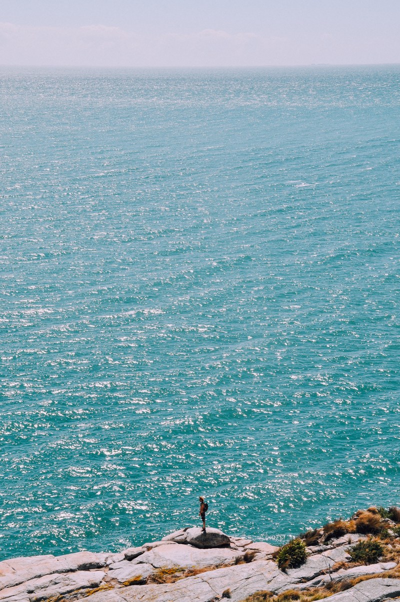 a hiker standing on a rocky ledge over the choppy sea stretching to the horizon, ledge over the azure sea 4k