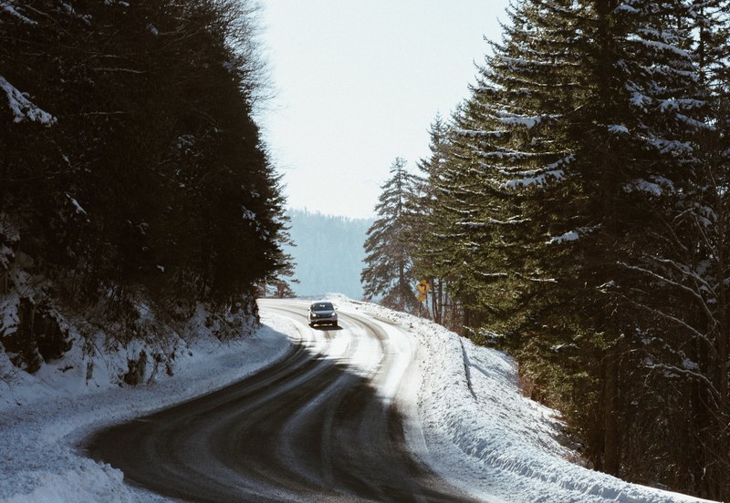 car driving down shoveled road between trees, snowy winding road 4k