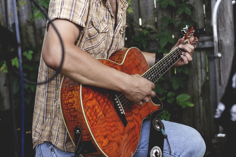 a man in a checkered shirt strumming an acoustic guitar in a garden, guitar player in a garden 4k