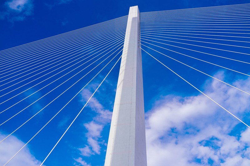 engineering details of a white suspension bridge on a cloudy blue day, suspension bridge cables 4k