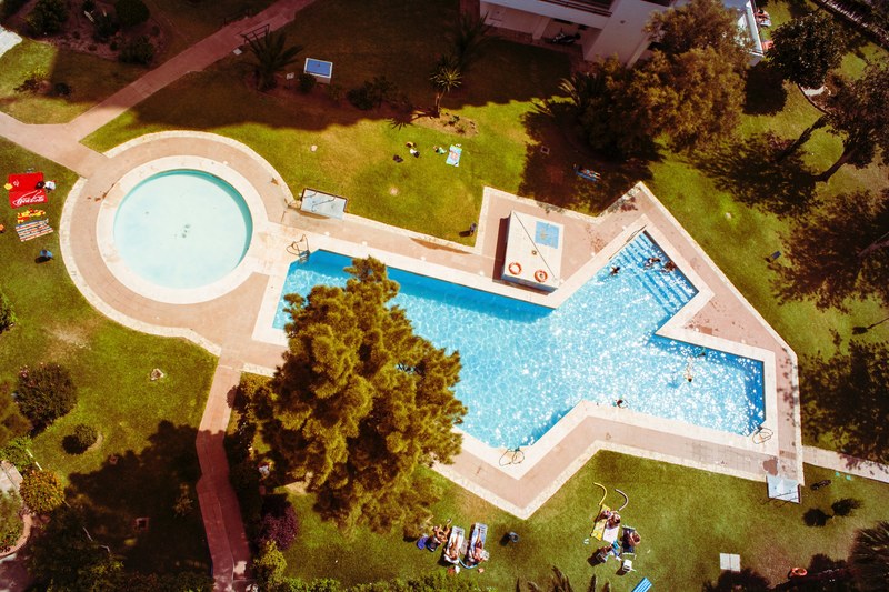 drone view of pool in shape of x and o with swimming and sunbathing people, drone pool x and o shape 4k
