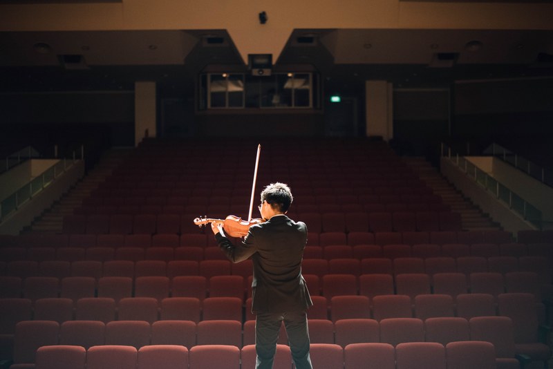 a man playing the violin on stage in front of an empty auditorium, rehearsing for the violin concert 4k