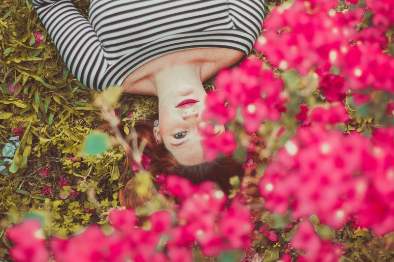a woman lying on her back in the grass with pink flowers over her head, lying among flowers 4k