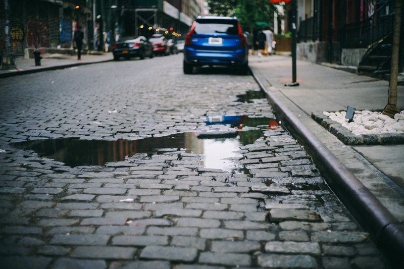 cobblestone street with parked car and puddle reflecting sky, cobblestone street 4k